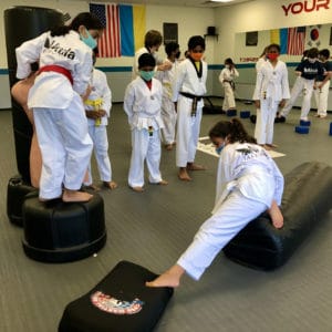 photo of a girl on a kicking bag stretching her leg to reach the next step of an obstacle course in her martial arts class